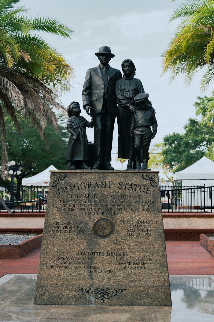 A monument honoring immigrants in Ybor City, Tampa, Florida under palm trees.